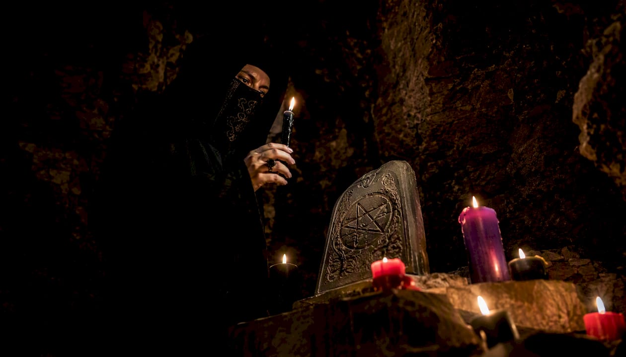 Hooded figure holding candle in dark ritual